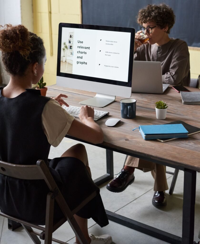 Two adults in an office discussing data on a computer screen.
